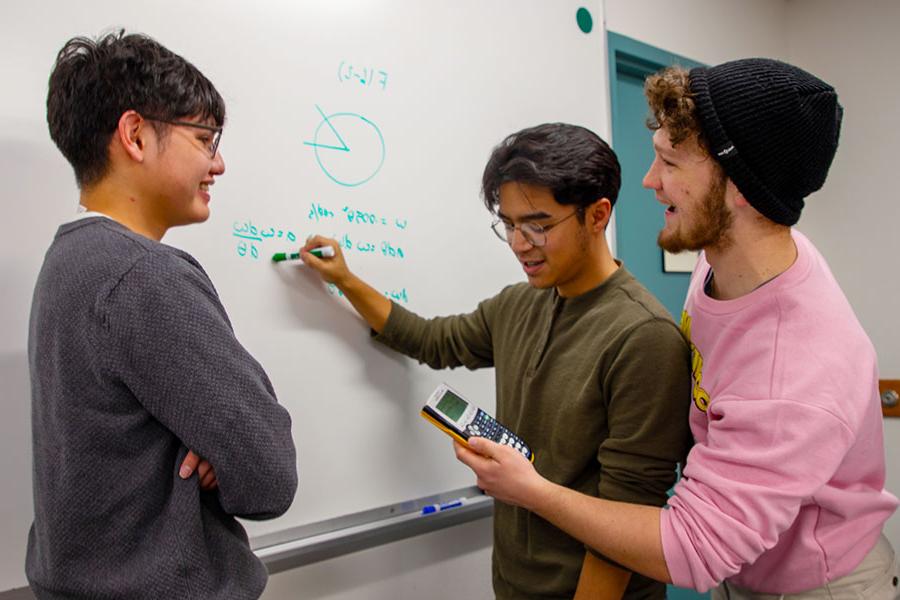 Three San Juan College students working on a math problem on a whiteboard